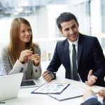 des personnes en costume-cravate et tailleurs discutent autour d'une table avec ordinateur, tablette et documents