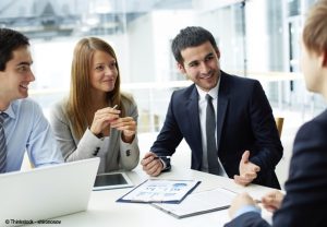 des personnes en costume-cravate et tailleurs discutent autour d'une table avec ordinateur, tablette et documents