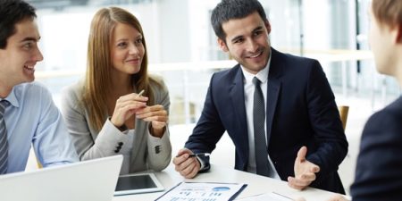 des personnes en costume-cravate et tailleurs discutent autour d'une table avec ordinateur, tablette et documents