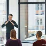 Un homme debout devant un paperboard en pleine explication face à un public d'adultes