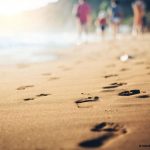 gros plan sur une plage de sable que des promeneurs en second plan ont foulée