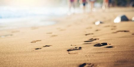 gros plan sur une plage de sable que des promeneurs en second plan ont foulée