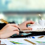 une main équipée d'un crayon, avec une calculette et un agenda à côté