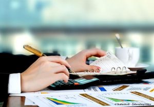 une main équipée d'un crayon, avec une calculette et un agenda à côté