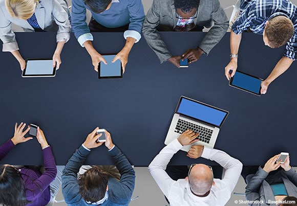 des personnes autour d'une table utilisent smartphones, tablettes, et ordinateurs évoquant l'utilité d'une charte informatique