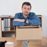 un homme accoudé à un grand carton posé sur un bureau comme s'il était licencié pour maladie