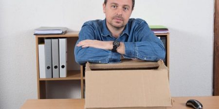 un homme accoudé à un grand carton posé sur un bureau comme s'il était licencié pour maladie