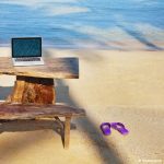 un ordinateur posé sur le bout d'une table installée sur une plage des tropiques