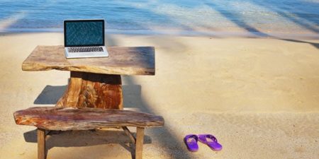 un ordinateur posé sur le bout d'une table installée sur une plage des tropiques