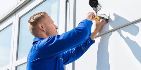 un homme en bleu de travail installe une caméra extérieure