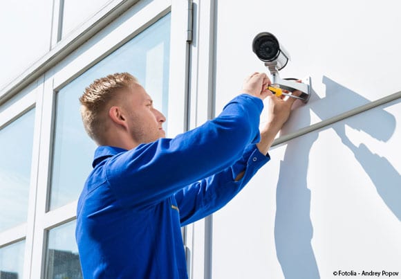 un homme en bleu de travail installe une caméra extérieure