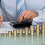 un homme derrière des piles de pièces de monnaie avec papier, calculette et crayon