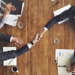 Deux mains de part et d'autre d'une table se serrent en symbole de la transmission d'entreprise à un associé