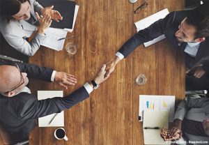 Deux mains de part et d'autre d'une table se serrent en symbole de la transmission d'entreprise à un associé