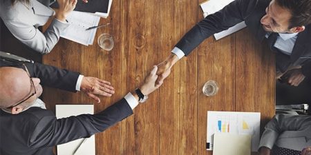 Deux mains de part et d'autre d'une table se serrent en symbole de la transmission d'entreprise à un associé