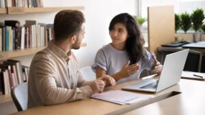 Manager expliquant une fiche de paie à une salariée lors d’un entretien avec documents et ordinateur portable