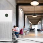 Purificateur d’air blanc posé sur une table en marbre dans un espace de travail moderne et lumineux, avec des personnes floues en arrière-plan.